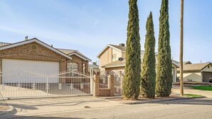Uma rua residencial com casas, um portão de entrada e altas ciprestes.