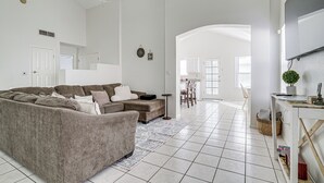 Uma sala de estar ampla com sofá seccional, ventilador de teto e área de jantar ao fundo.