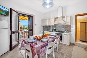 A modern kitchen with a dining area, a TV mounted on the wall, and a view of the outdoors.