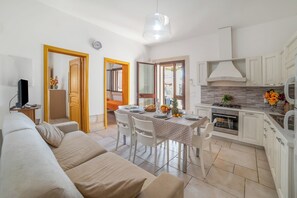 A modern living room with a sofa, dining table, and kitchen area with cabinets and a stove. - Villa Gloria and Marta With Garden Near The Sea (Melendugno)