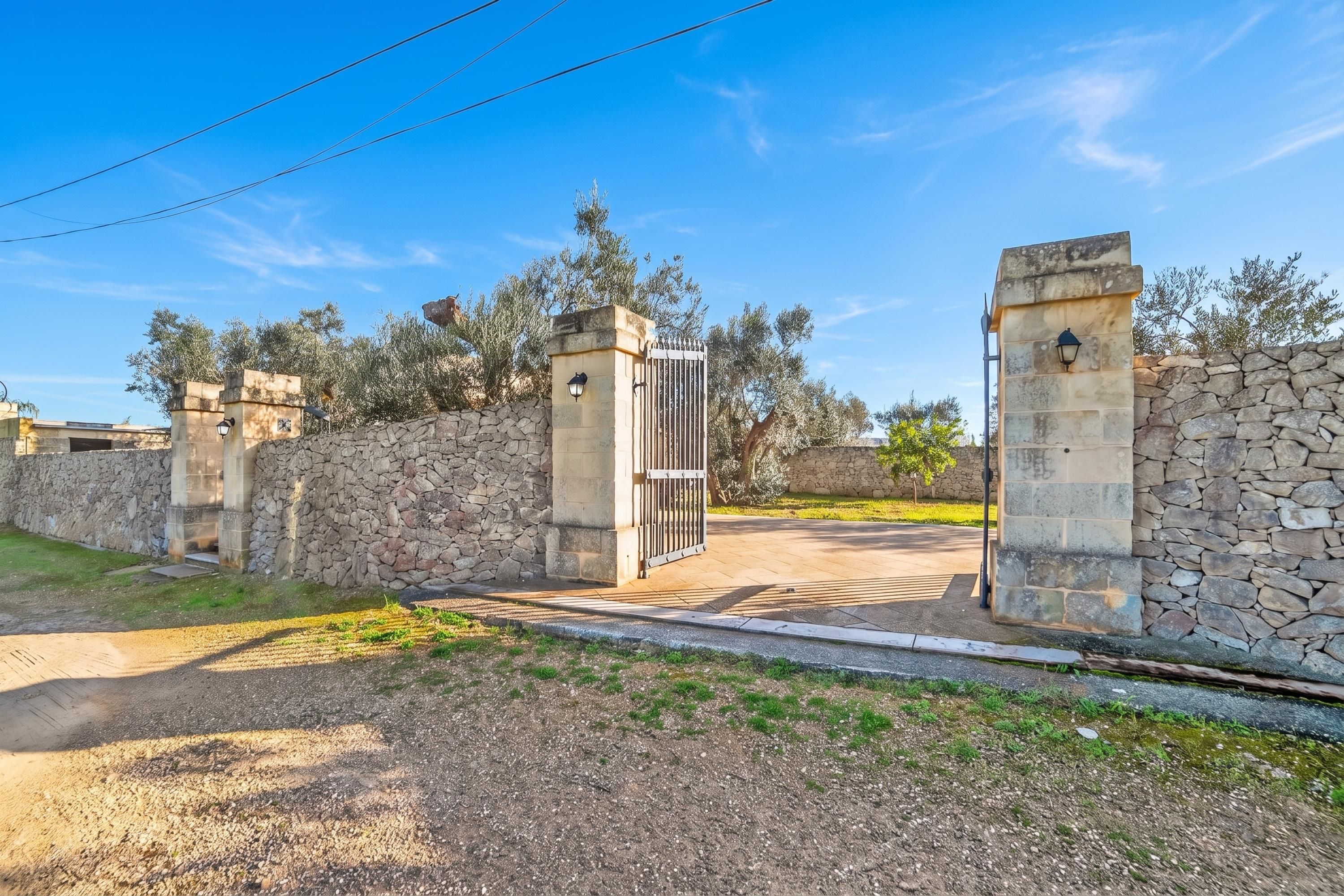 A gated entrance with stone walls and a metal gate, leading to a paved driveway.