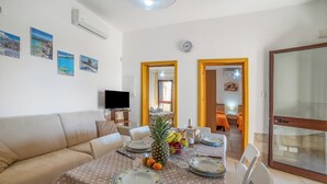 A dining area with a table set for four, a sofa, a TV, and a view of a dining room with a table and chairs.