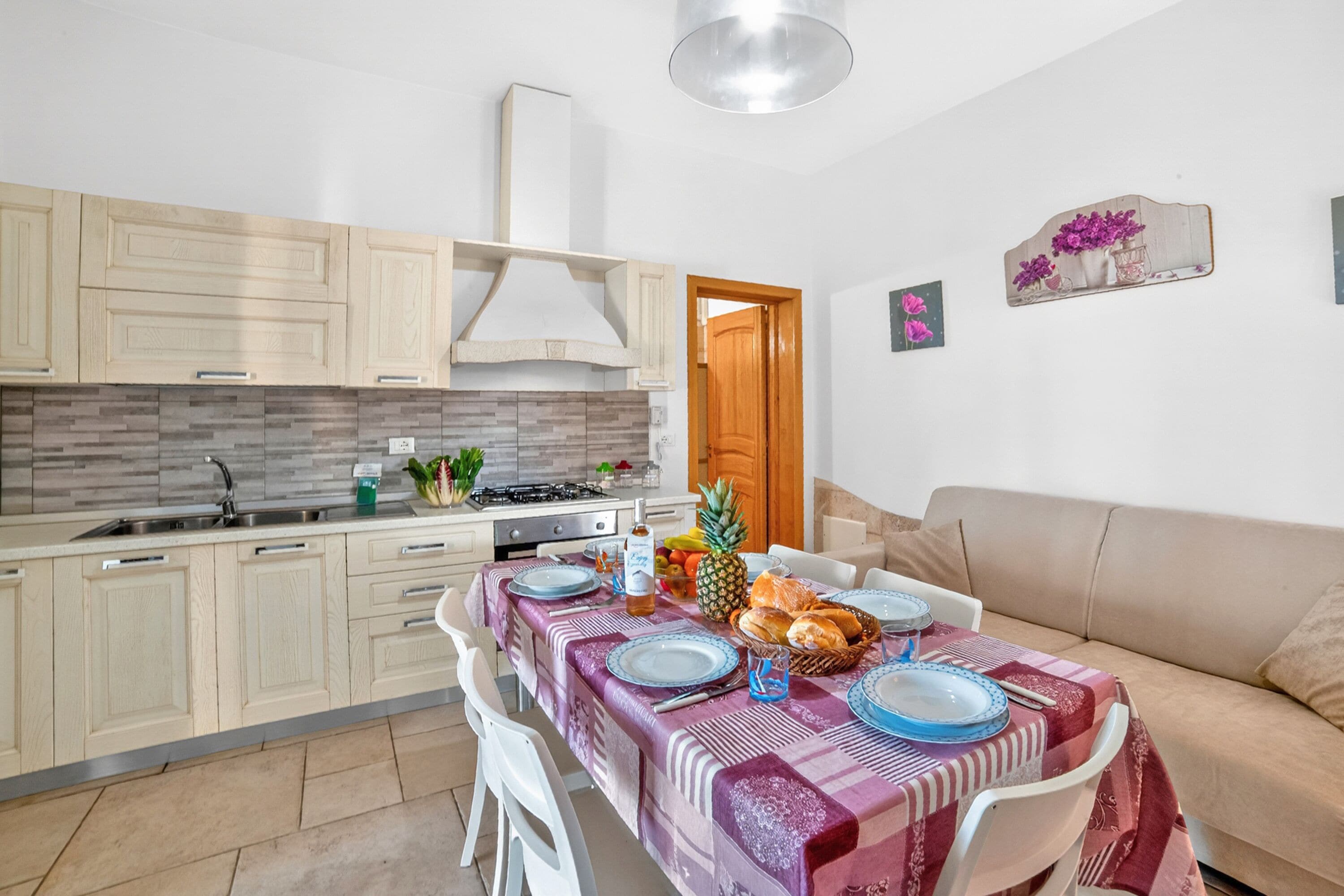 A modern kitchen with light wooden cabinets, a stainless steel sink, and a dining area with a table set for four.