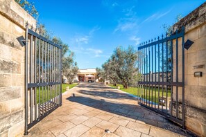 A gated entrance to a property with a paved pathway leading to a building with a covered patio area. - Villa Gloria and Marta With Garden Near The Sea (Melendugno)