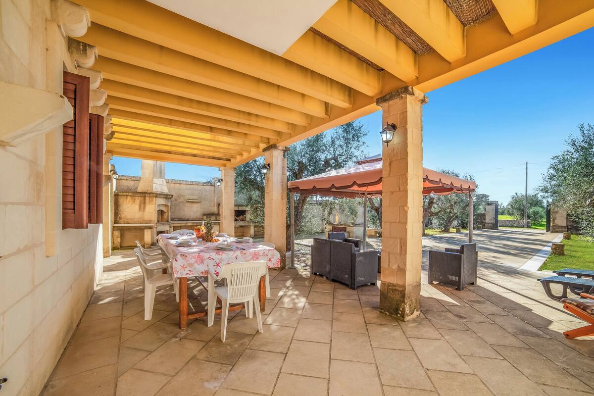 An outdoor patio with a table and chairs, a grill, and a covered seating area.