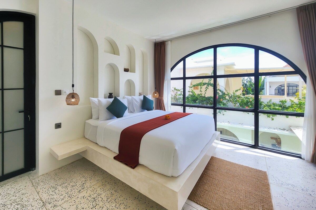 Ein modernes Schlafzimmer mit einem großen Bett und Blick auf grüne Natur, versehen mit einem einzigartigen Bogenfenster.