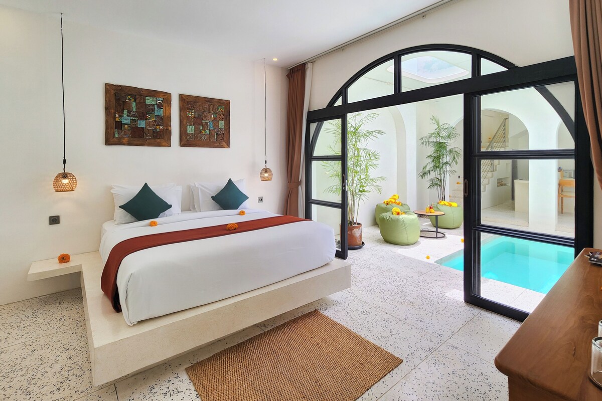 Ein modernes Schlafzimmer mit einem großen Bett, Blick auf einen Swimmingpool und zwei Kunstwerken an der Wand.