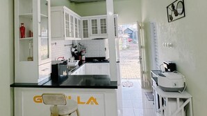 A kitchen with white cabinets, a black countertop, and a stool. There is a small table with a printer and a wall-mounted mirror. - Homestay Gavilla Dieng (Kejajar)