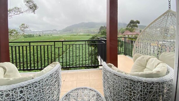 A balcony with wicker chairs and a hanging chair, overlooking a green landscape and distant hills. - Homestay Gavilla Dieng (Kejajar)