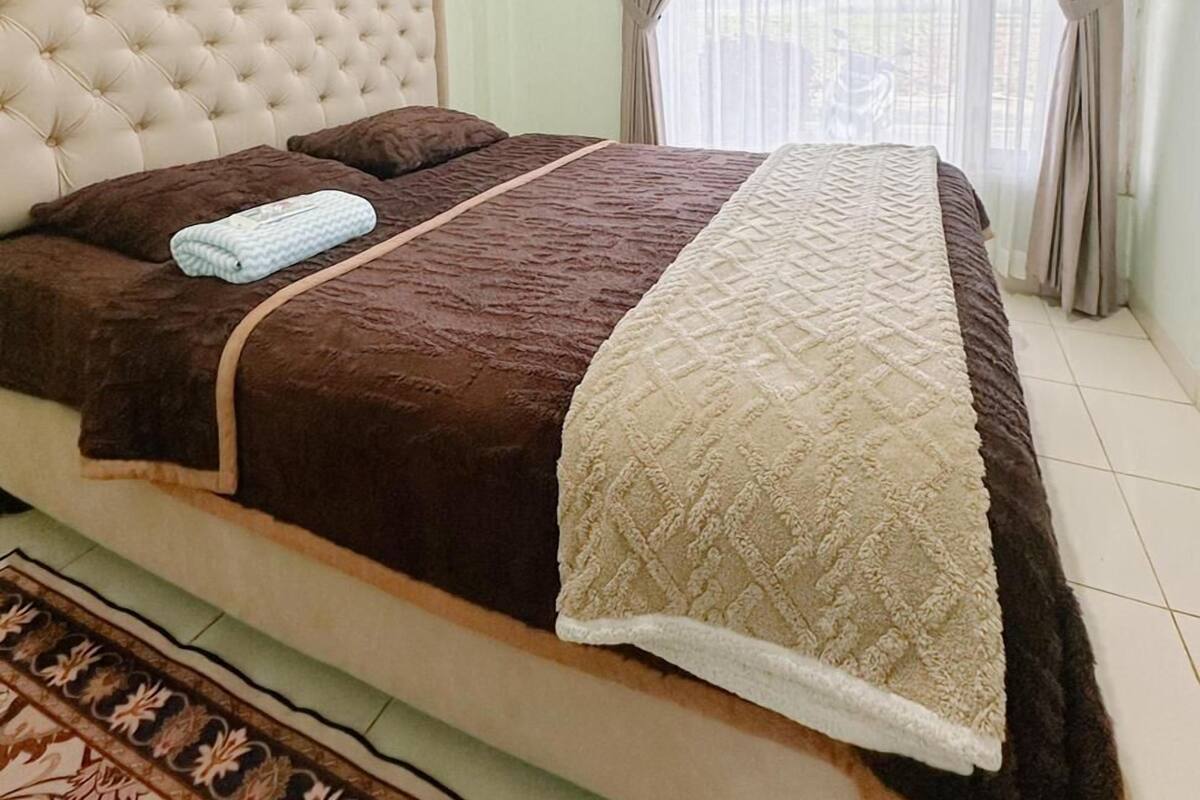 A bedroom with a large bed, a headboard, and a window with curtains.