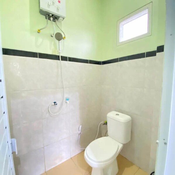 Et lille badeværelse med toilet, brusebad og et vindue.