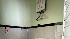 A small bathroom with a toilet, a shower, and a wall-mounted water heater. - Homestay Gavilla Dieng (Kejajar)
