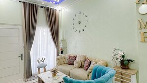 A modern living room with a blue armchair, a beige sofa, a small table, and a clock on the wall. - Homestay Gavilla Dieng (Kejajar)