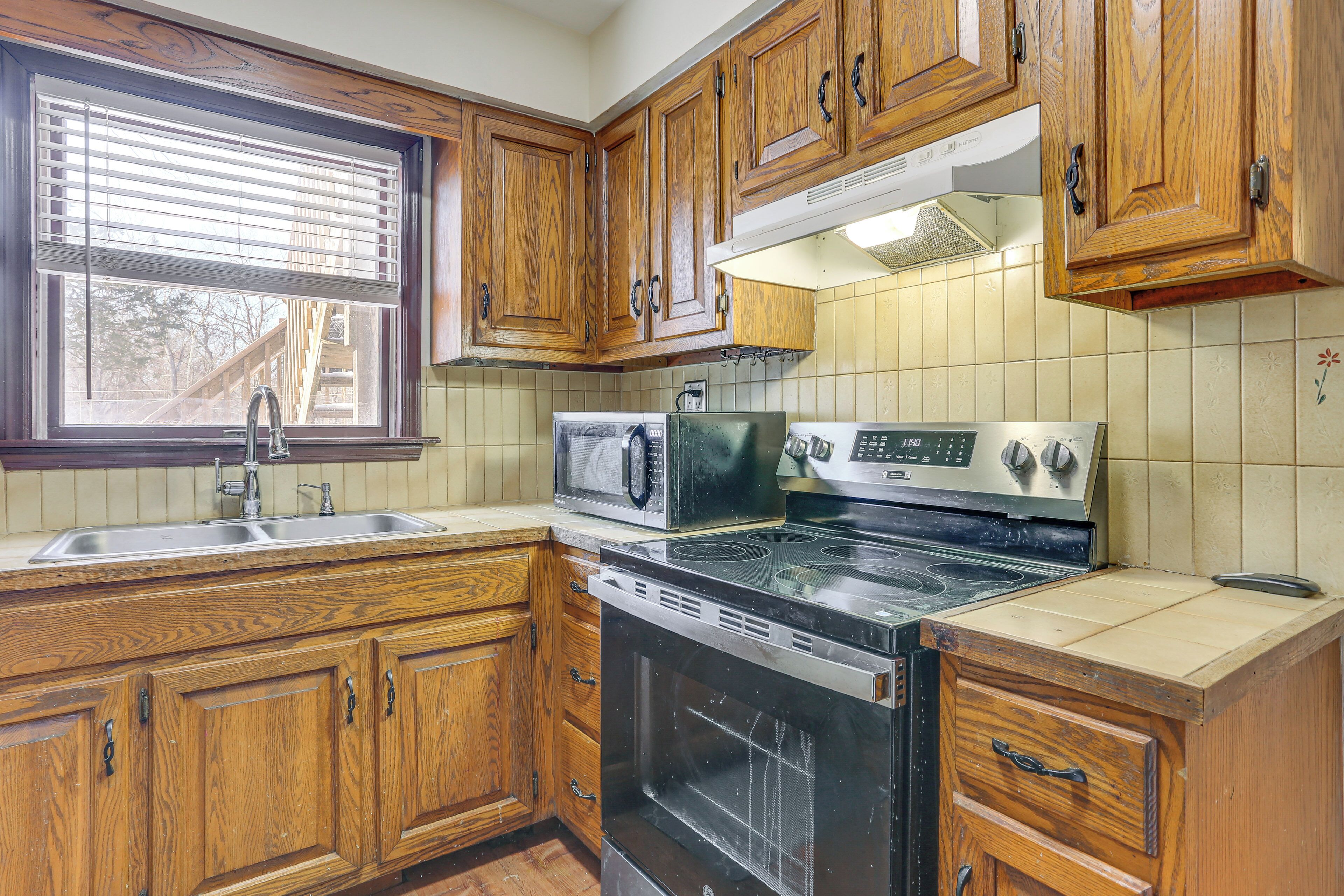 A kitchen with wooden cabinets, a stove, a microwave, and a sink.