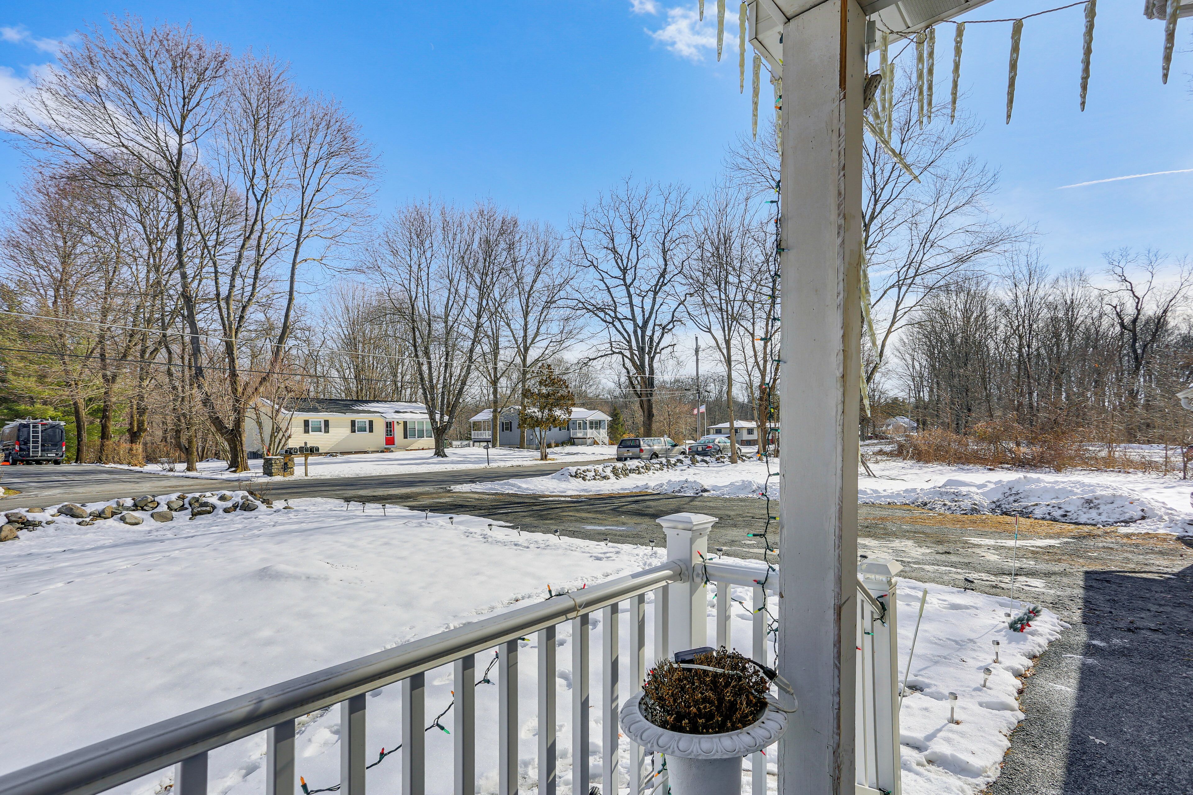 A residential area with a snow-covered driveway, a white railing, and a house in the background.