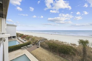 Une propriété située en bord de mer, dotée d’une piscine, d’une terrasse en bois et offrant une vue sur la plage et l’océan.