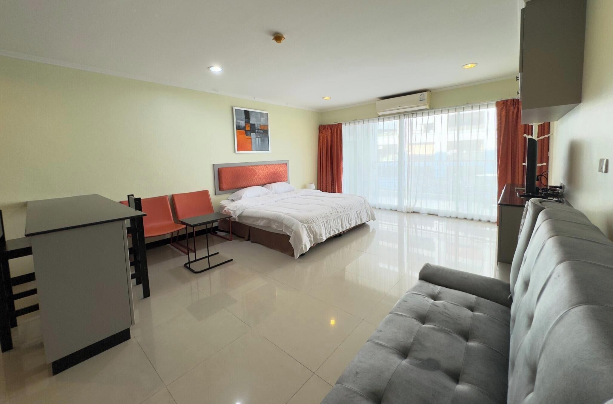 A hotel room with a bed, a desk, two chairs, a sofa, and a large window with curtains.