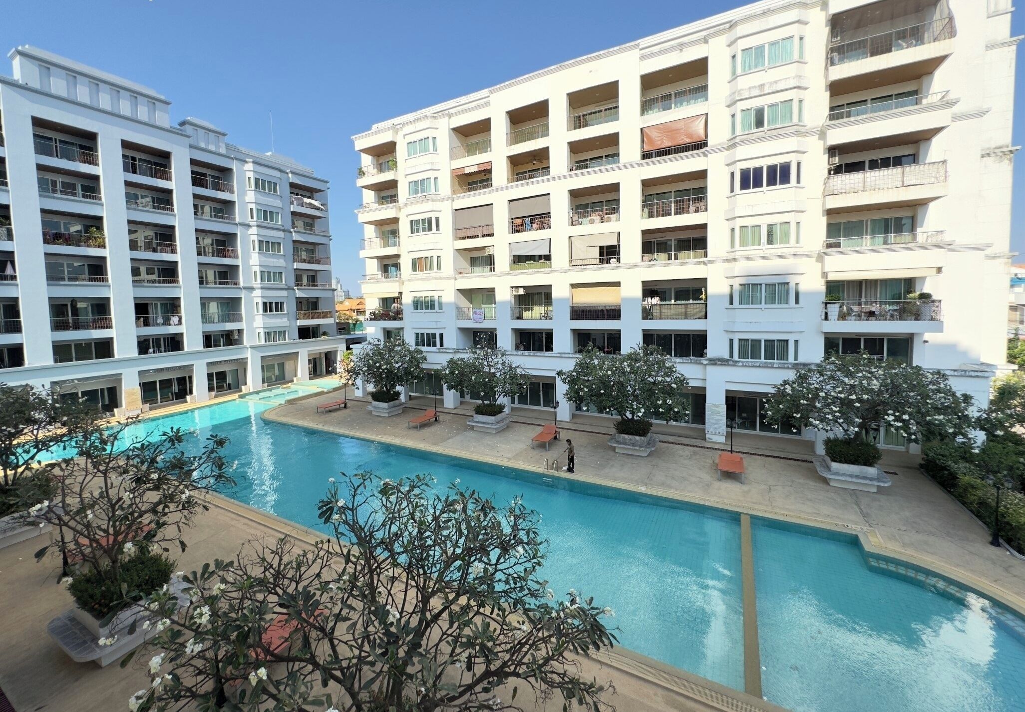 A multi-story hotel with a central swimming pool surrounded by potted plants and outdoor seating.