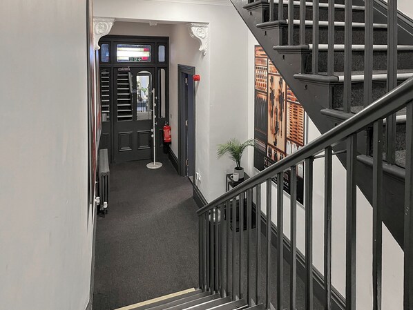 Un couloir avec un escalier, une porte dotée d’une fenêtre, un extincteur et une petite plante posée sur une table.