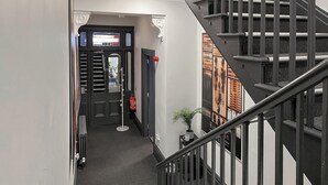 A hallway with a staircase, a door with a window, a fire extinguisher, and a small plant on a table. - 8 bedroom accommodation in Sunderland (Sunderland)