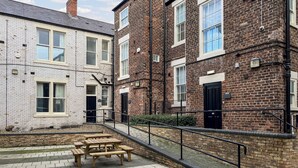A courtyard with picnic tables, a brick building with windows, and a white building with a tiled roof. - 8 bedroom accommodation in Sunderland (Sunderland)