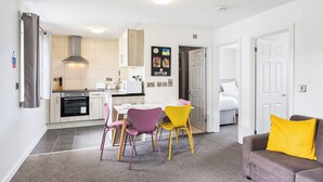 Een knus woongedeelte met een kitchenette, een eethoek en een bank met een geel kussen.