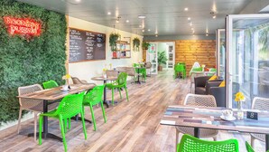 A restaurant with green chairs, wooden tables, a neon sign, a menu board, and a wooden wall.