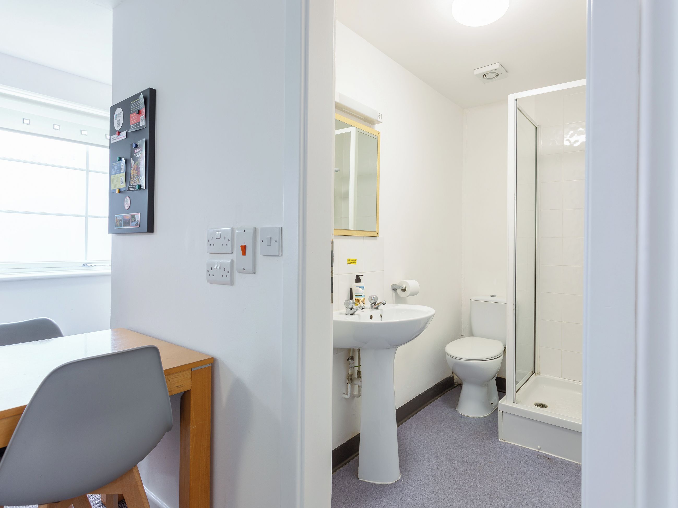 A room with a desk, chair, white walls, a sink, toilet, and a shower.