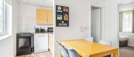 A compact kitchen with a dishwasher, oven, and microwave. There is a wooden dining table with chairs.
