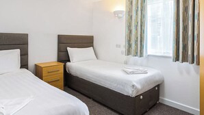 Ein Hotelzimmer mit zwei Betten, einem Holzkasten, einem Fenster mit Vorhängen und einer Wandleuchte.