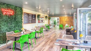 Ein Restaurant mit grünen Stühlen, Holztischen, einer Neonreklame, einer Speisekarte und einer Holzwand.