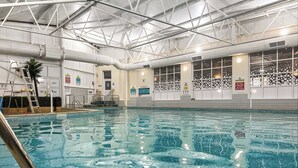 Ein Hallenbad mit klarem Wasser, einer Metallleiter und Sicherheitshinweisen an den Wänden.