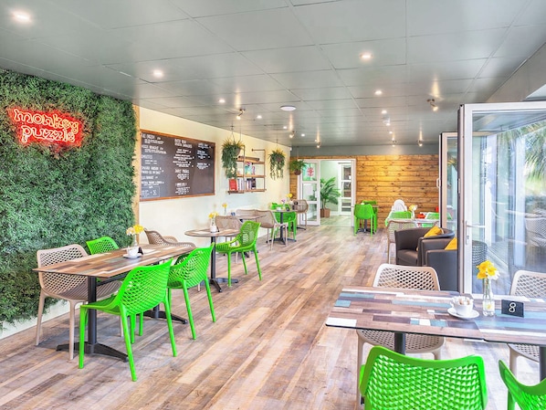 Un café con sillas verdes, mesas de madera, un letrero de neón, una pizarra de menú y una pared de madera.