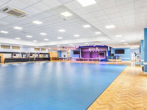 A spacious indoor area with a blue floor, a reception desk, and a stage with a sign reading 'North Devon'. - 5T Monk's Rock - UKC8995 (Illfracombe)