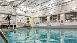 An indoor swimming pool with clear water, a metal ladder, and safety signs on the walls.