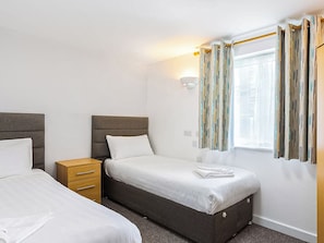 Habitación de hotel con dos camas, un aparador de madera, una ventana con cortinas y una lámpara fijada a la pared.