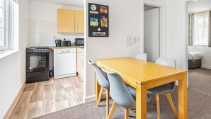 A compact kitchen with a stove, microwave, and dishwasher. A dining table with chairs is in the adjacent room.