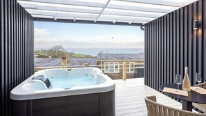 Una vasca idromassaggio su un pontile in legno con vista sul mare e sugli edifici.