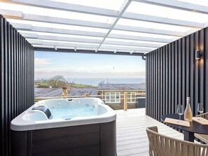 A hot tub on a wooden deck with a view of the sea and buildings. - 178 Residences - UKC8998 (Illfracombe)