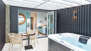 A modern outdoor patio with a hot tub, wicker chairs, and a glass door leading to an interior living area. - 177 Residences - UKC8999 (Illfracombe)