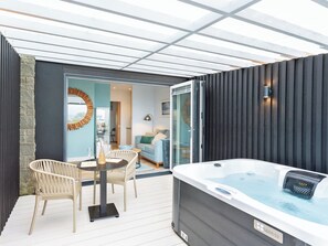 Eine moderne Außenpatio mit Whirlpool, Korbstühlen und einer Glastür zu einem Wohnbereich.