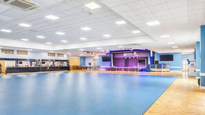 A spacious indoor area with a blue floor, a reception desk, a stage with a banner, and a large screen. - 177 Residences - UKC8999 (Illfracombe)