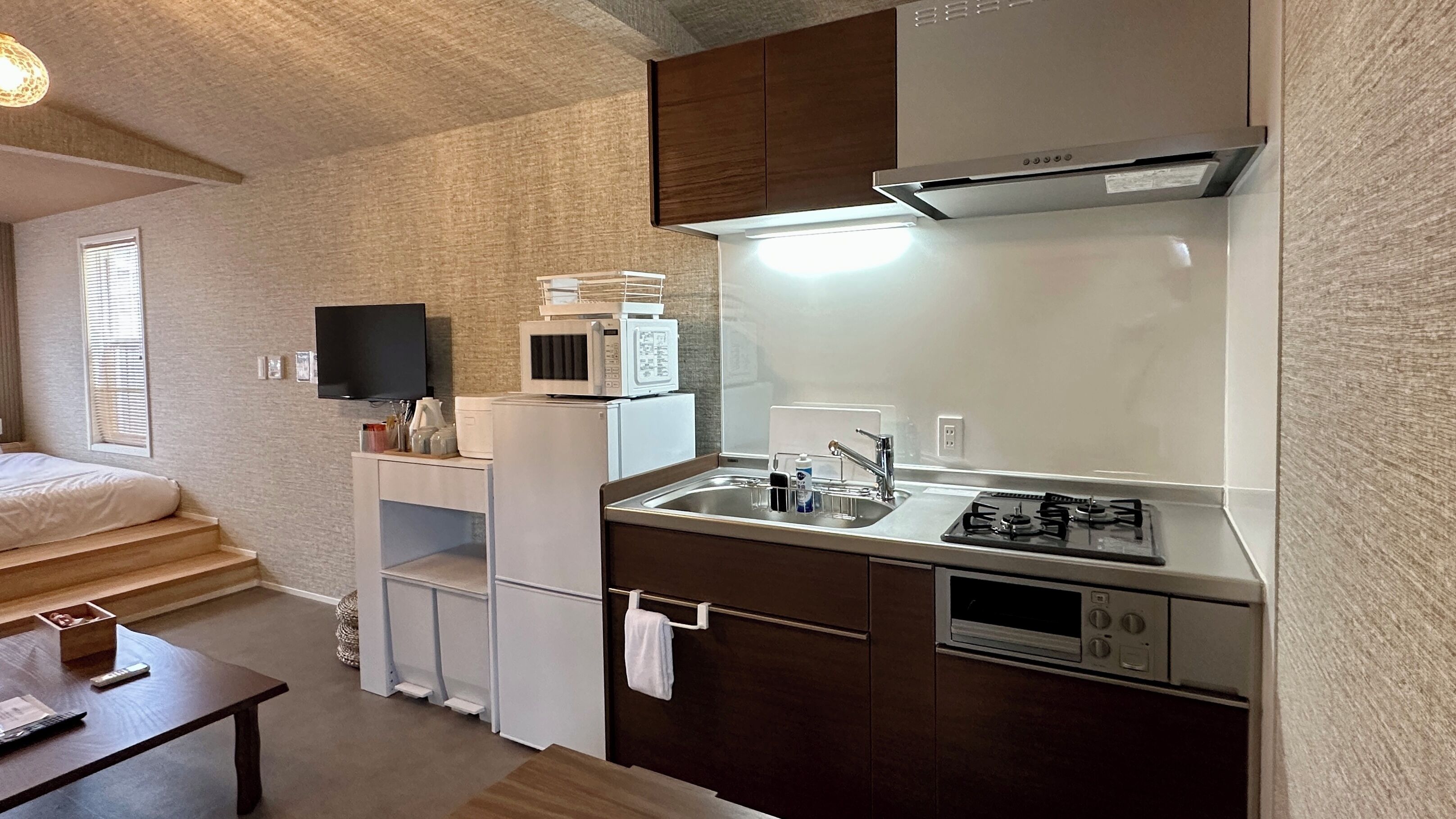 A compact kitchen with a microwave, stove, and sink. There is a small seating area with a table and a TV mounted on the wall.