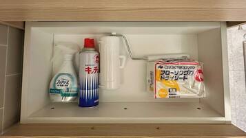 Un estante de baño con una botella de jabón líquido, un ambientador en aerosol, un pulverizador y un paquete de papel higiénico.
