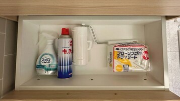 Un estante de baño con una botella de jabón líquido, un ambientador en aerosol, un pulverizador y un paquete de papel higiénico.