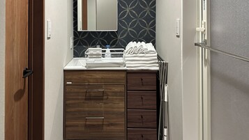 Un baño con tocador de madera, espejo, toallero y lavamanos con dispensador de jabón.