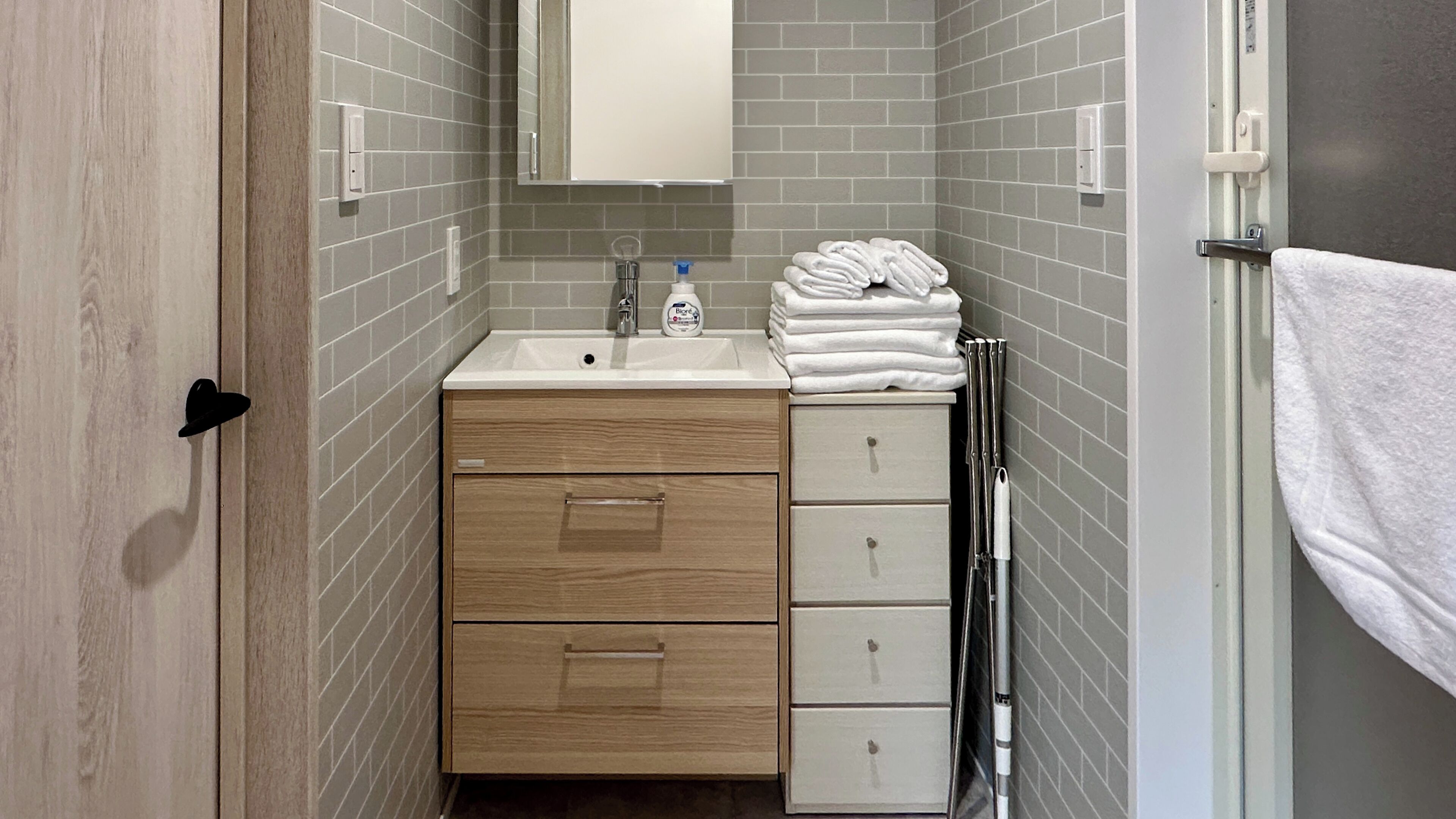 A bathroom with a wooden vanity, a sink, and a mirror. There are towels stacked on the right side.