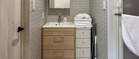 A bathroom with a wooden vanity, a sink, and a mirror. There are towels stacked on the right side.