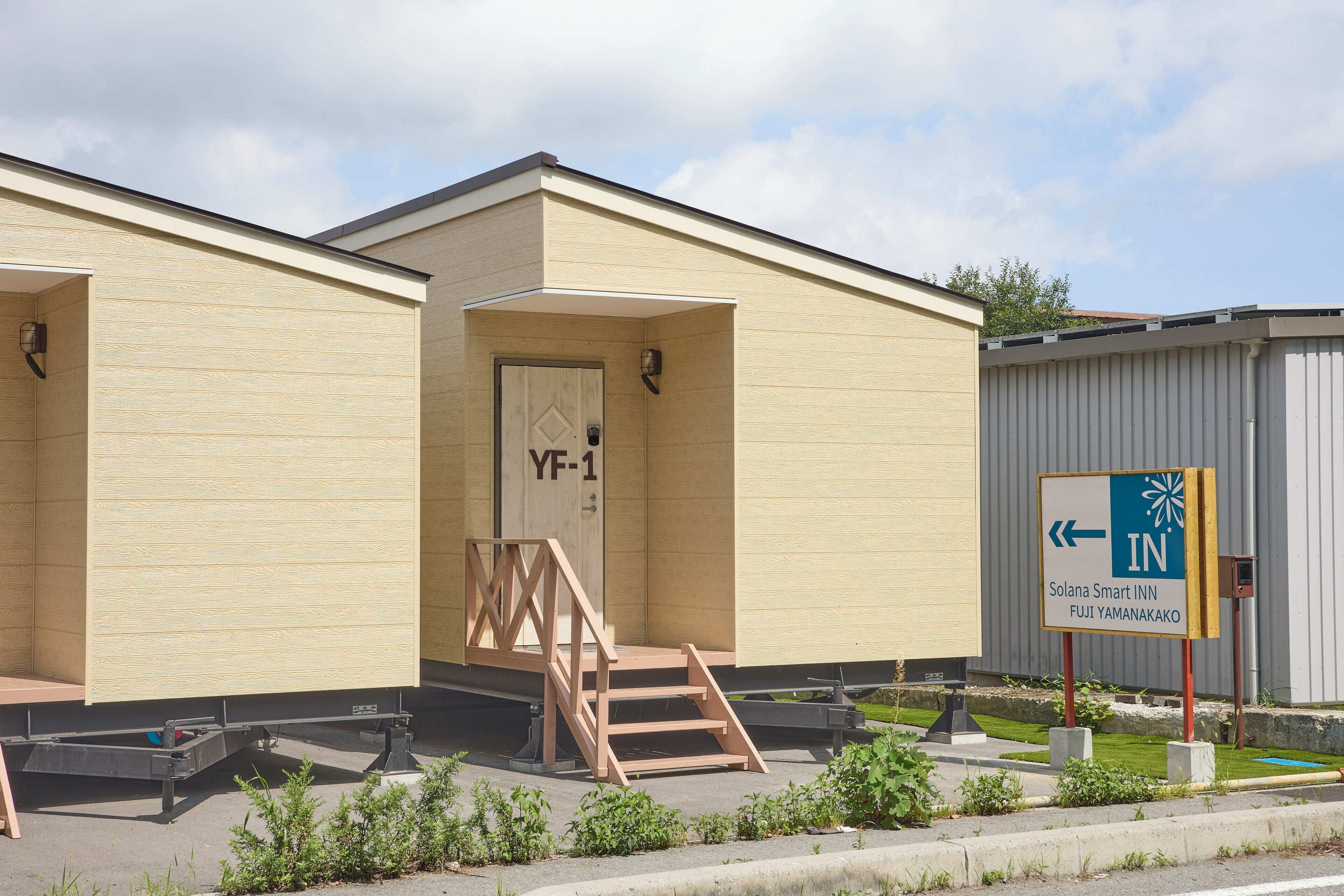 A hotel with a beige exterior, a wooden door labeled "YF-1", and a sign indicating the direction to the Solana Smart Inn in Fuji, Yamanakako.