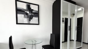 Ein modernes Zimmer mit einem Glastisch, zwei schwarzen Stühlen, einem schwarz-weißen abstrakten Gemälde und einem großen Spiegel mit schwarzem Rahmen.